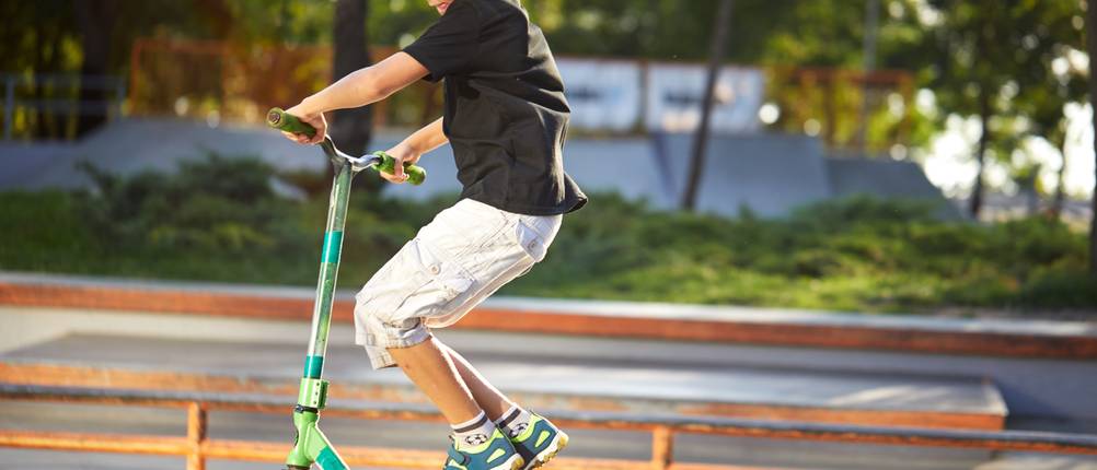 Stunt-Scooter-Test: Junge mit Schutzhelm, der in einem Skatepark kleine Kunststücke mit seinen Roller durchführt
