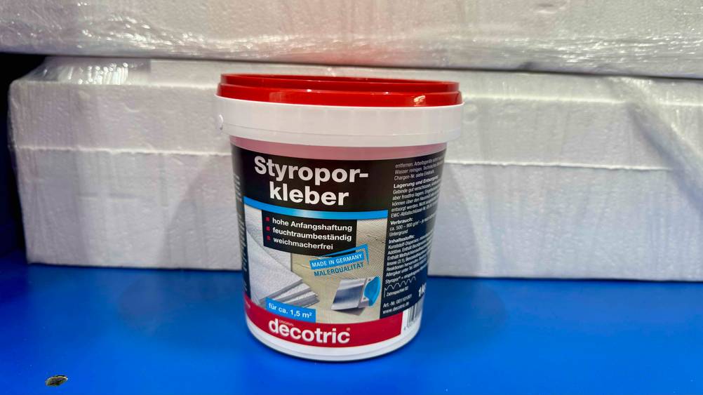 Vor Styropor steht der getestete Styroporkleber auf einer blauen Fläche.