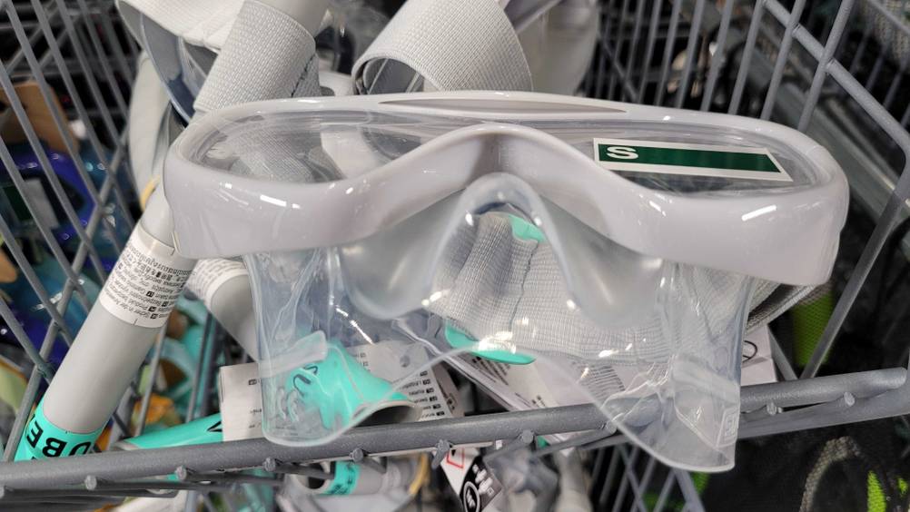 Nahaufnahme eines hellgrauen Kinder-Schnorchelsets im Test, in der Größe S, mit Fokus auf das integrierte Trockenschnorchel-System mit Spritzwasserschutz, in einem Verkaufsbereich.