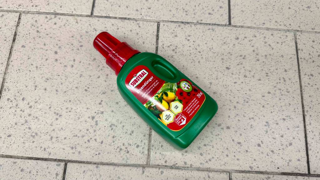 Eisendünger-Test: Eine grüne Kunststoffflasche inklusive Dosierkappe liegt auf einem Fliesenboden.