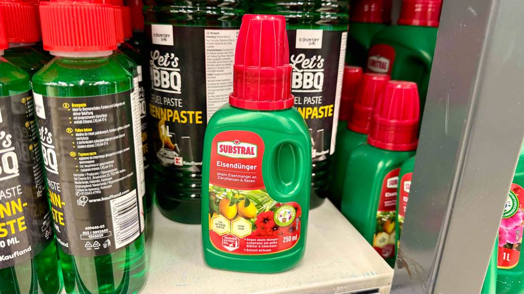 Auf einem Verkaufsregal steht getesteter Eisendünger in der grünen Kunststoffflasche inklusive roter Dosierkappe neben weiteren Substraten.