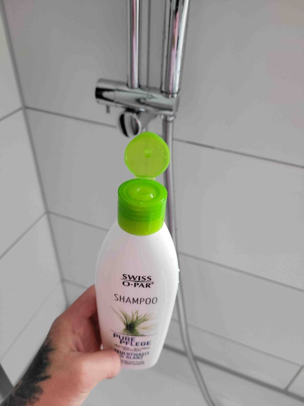 Nahaufnahme der Verschlusskappe eines getesteten sulfatfreien Shampoos von einer Hand in der Dusche gehalten.