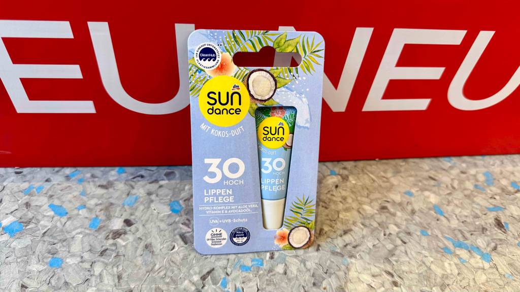 Im Test: Lippenpflege mit Sonnenschutz 30 steht in seiner Verpackung vor einem roten Plakat.