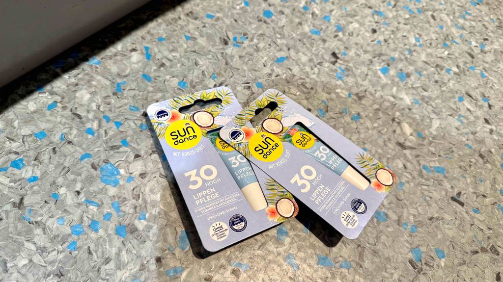 Getestete Lippenpflege mit Sonnenschutz 30 liegt auf einem Linoleumbelag innerhalb zweier Verpackungen.