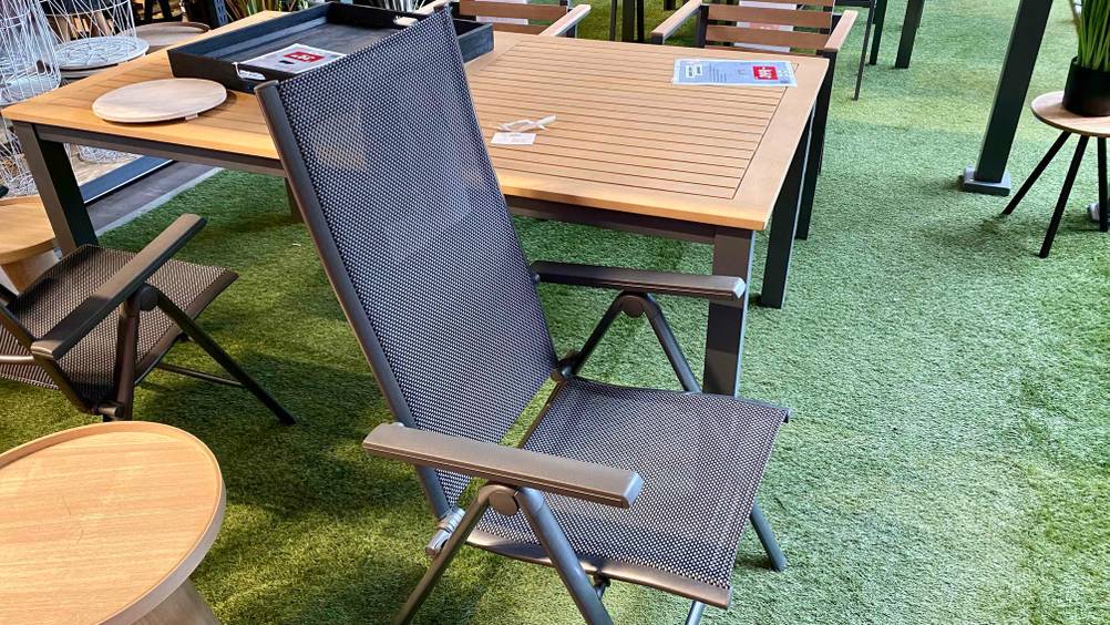 Im Test: Ein Alu-Klappsessel von der Seite vor einem Tisch auf einer grünen Fläche.