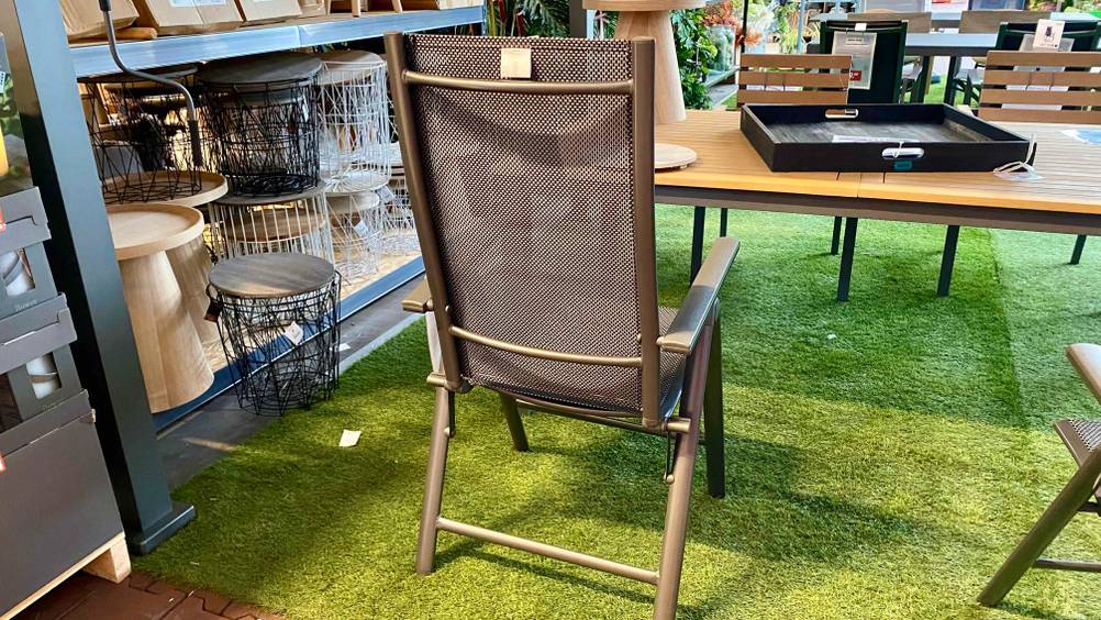 Alu-Klappsessel-Test: Ein Stuhl von hinten an einem Tisch in einer Ausstellung stehend.