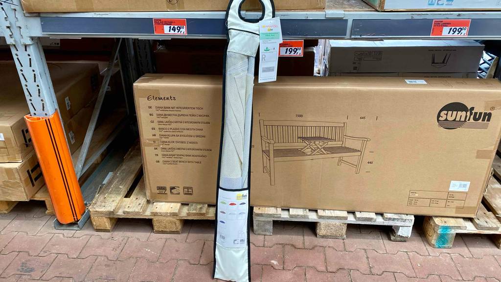 Ein verpackter Sonnenschirm mit 200 cm steht zum testen vor einem Verkaufsregal für Gartenmöbel.