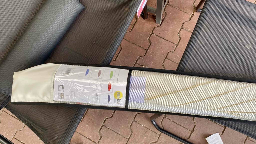 Getestet: Ein verpackter heller Sonnenschirm mit 200 cm liegt quer auf Stühlen.