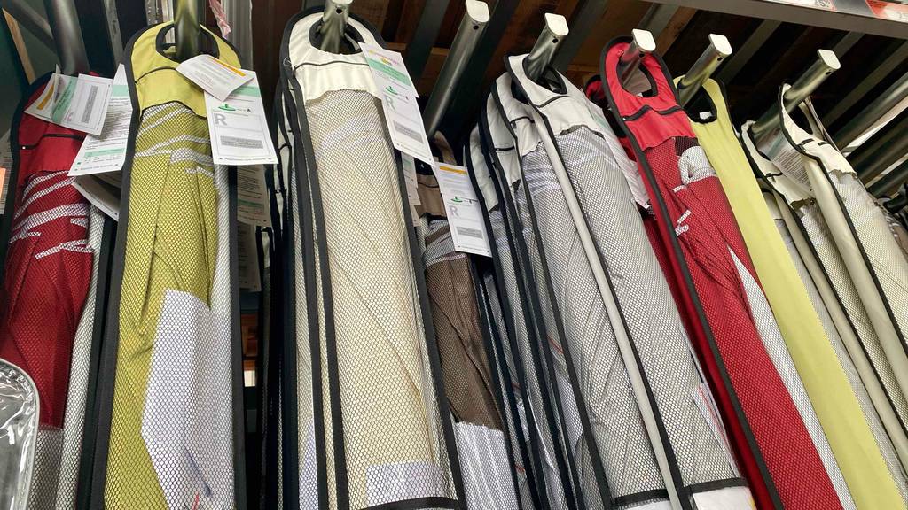Sonnenschirm 200 cm im Test: Mehrere Sonnenschirme in verschiedenen Farben hängen verpackt neben- und hintereinander in einem Verkaufsregal.