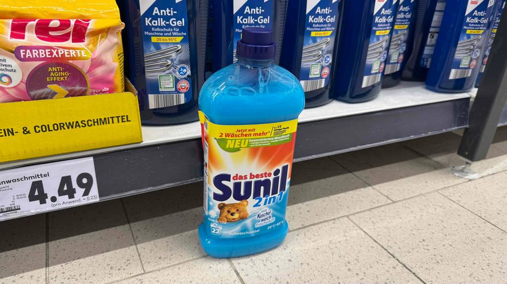 Eine Flasche mit getestetem, flüssigem Vollwaschmittel steht vor einem Waschmittel-Regal.