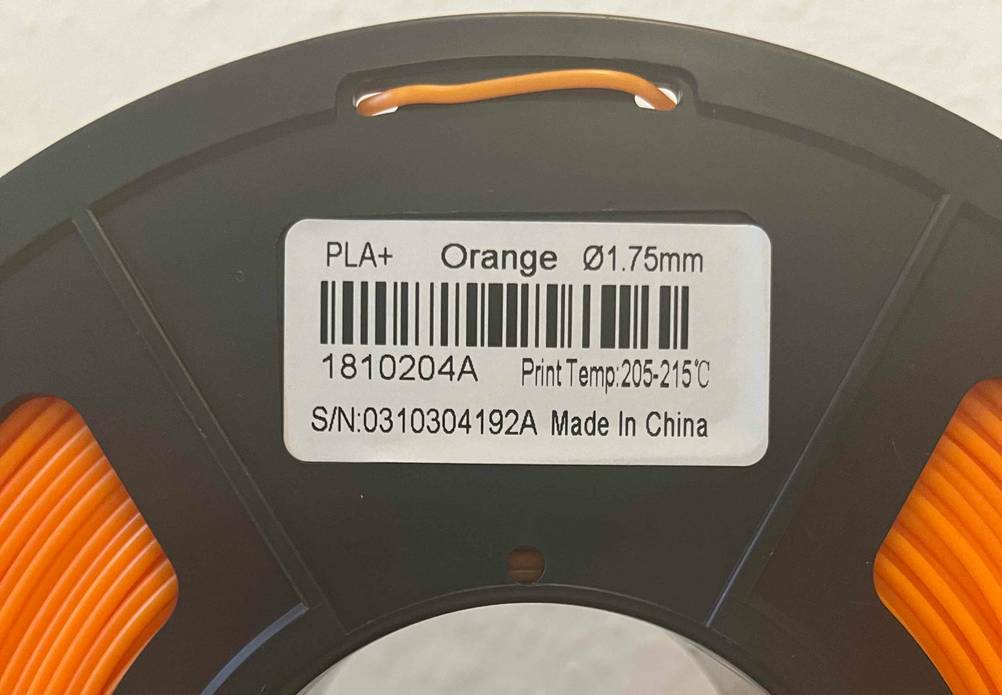 Nahaufnahme einer getesteten 3D-Drucker-Filament-Rolle mit orangem Drucker-Faden und Etikett mit Produktinformationen.