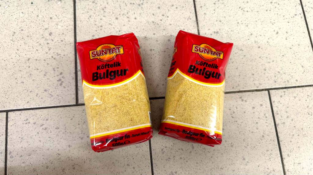 Bulgur im Test: Zwei 500-g-Packungen mit Sichtfenstern liegen auf einem Fliesenbelag.