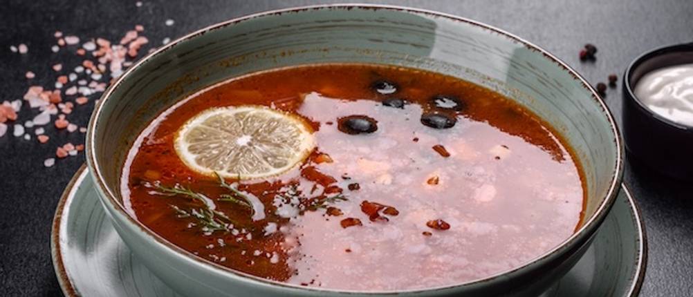 Keramik als Material getestet: Ein blau-grauer Suppenteller ist mit einer Tomatensuppe gefüllt, die mit Wacholderbeeren und Zitrone dekoriert ist.