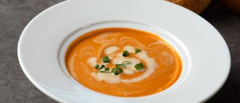 Suppenteller im Test: Ein einfacher weißer Porzellan-Suppenteller ist mit einer orangefarbenen Suppe gefüllt und mit etwas flüssiger Sahne und Petersilie garniert .