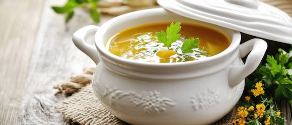 Suppenschüssel getestet: Auf einer Platzdecke steht eine weiße Suppenschüssel mit einer gelben Suppe. Der Deckel ist angehoben und schräg auf dem Rand der Schüssel abgestellt.