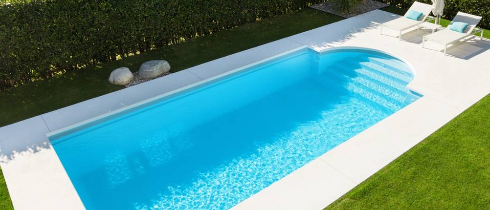 Ein großer Swimmingpool in einem Garten vor einer Hecke.