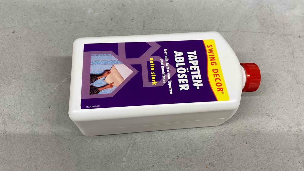 Im Test: Eine Flasche mit Tapetenablöser liegt quer auf einem grauen Boden.