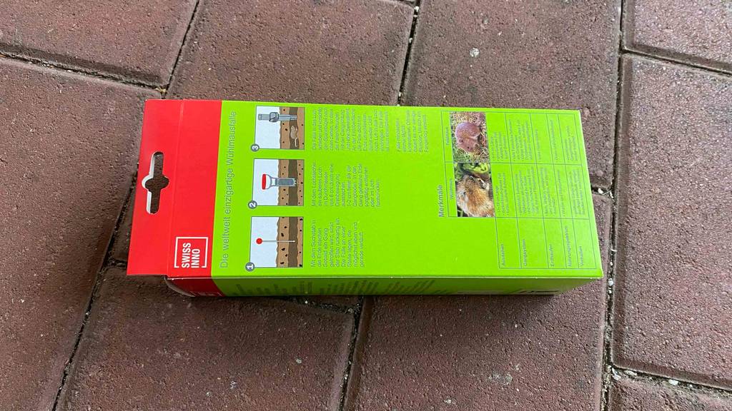 Wühlmausfalle im Test: Rückseite mit Anleitung einer Verpackung, die quer auf einem Pflasterboden liegt.