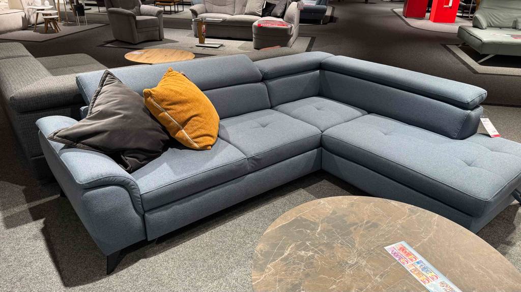Im Test: Ein Ecksofa mit grauem Stoffbezug steht von vorn betrachtet in einer Sofalandschaft im Geschäft.