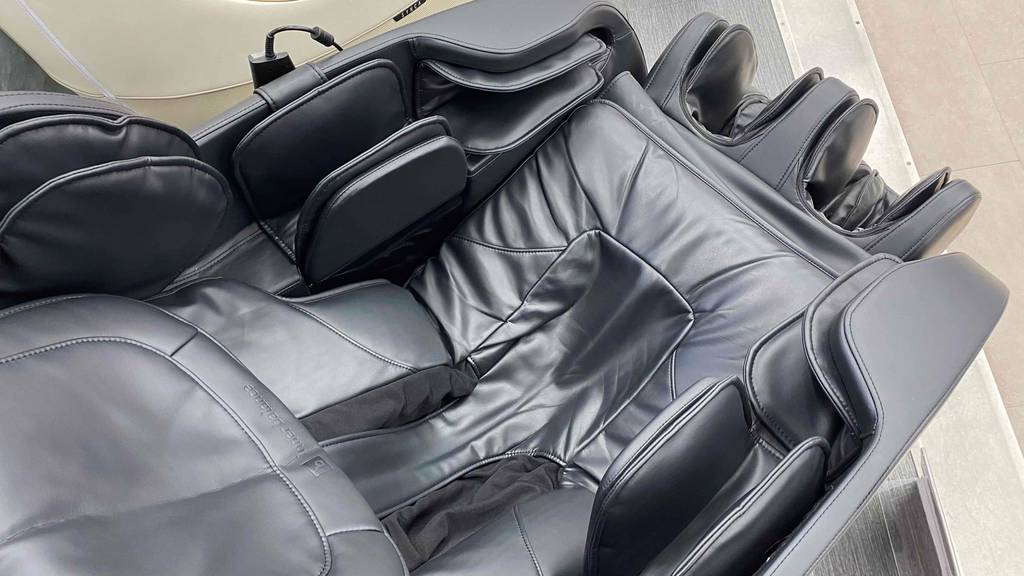 Detailansicht von oben auf den Sitz, die Armpositionen und die Beinablagen von einem schwarzen getesteten Massagesessel in Leder-Optik.