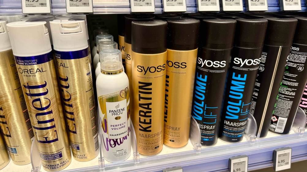 In einem Regal stehen mehrere Flaschen des getesteten Syoss-Haarsprays neben anderen Produkten.