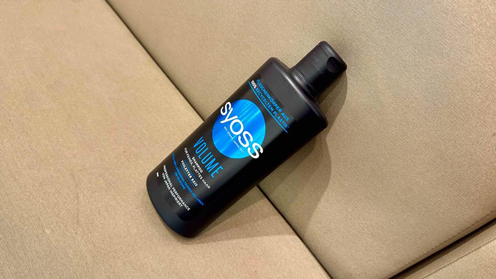 Eine Flasche des getesteten Syoss-Shampoos auf einem beigen Polster von schräg oben.