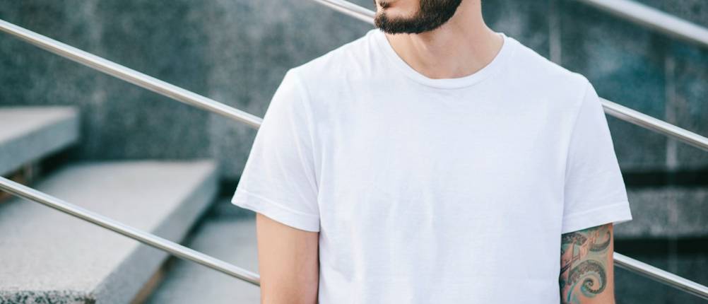 Ein junger Mann trägt draußen ein schlichtes weißes T-Shirt, ohne dass sein Gesicht zu sehen ist.