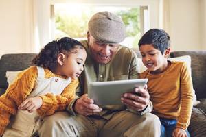 Tablet-Versicherungen im Test: Ein älterer Herr sitzt gemeinsam mit zwei Kindern auf einer Couch, während sie alle auf ein Tablet schauen.