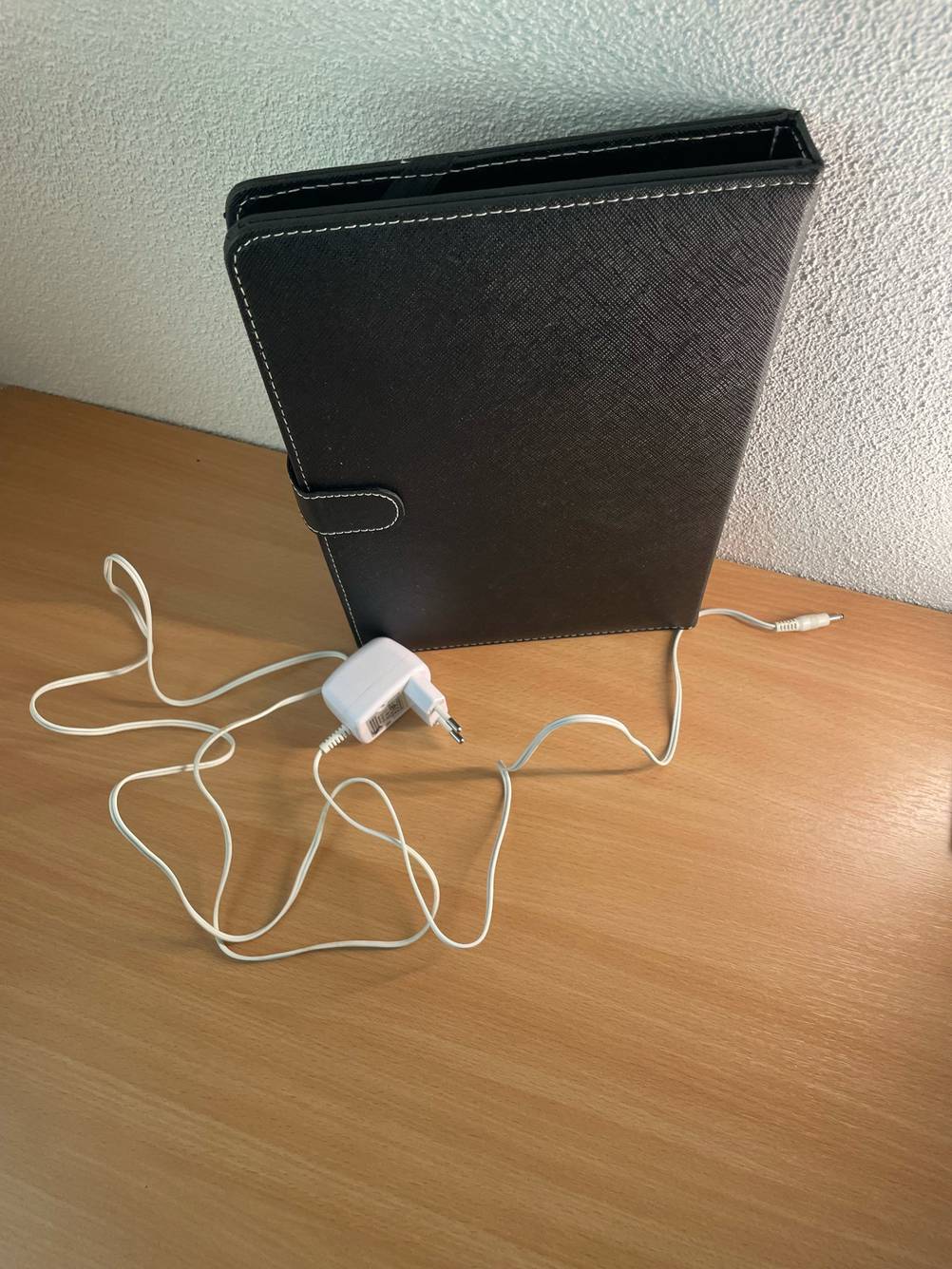 Ein getestetes Tablet bis 300 Euro eingepackt in einer Lederhülle mit Stromkabel auf einem Holztisch.