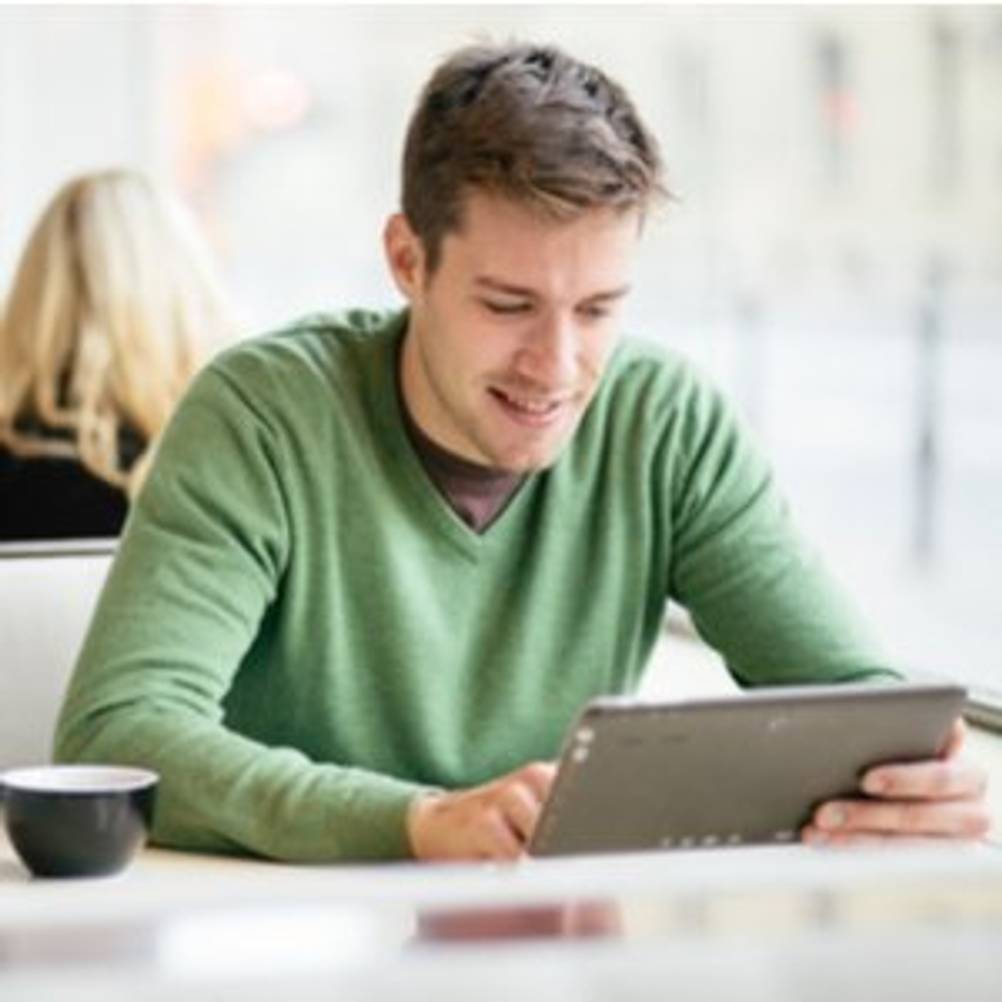 Junger Mann, der in einer Cafeteria sitzt und an einem Tablet arbeitet
