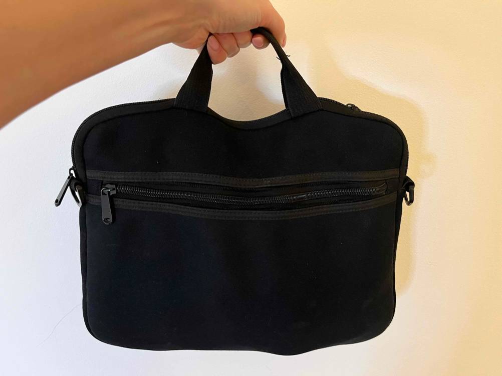 Im Test: Hand hält schwarze Tablet-Tasche an Tragegriff vor weißer Wand.