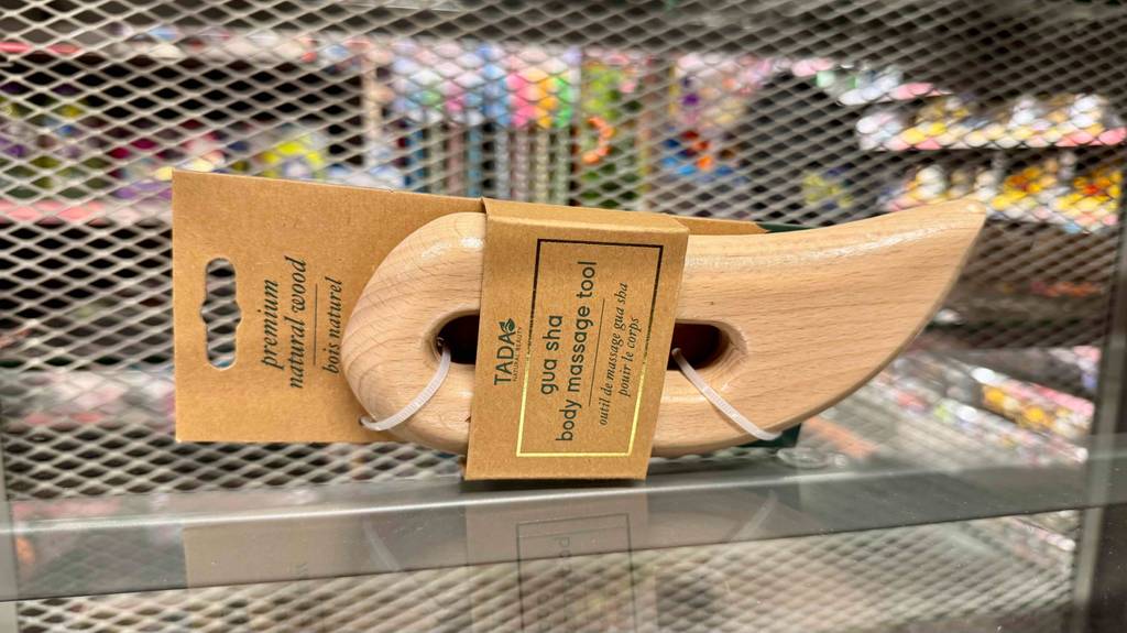 Gua Sha im Test: Ein geglättetes Holzstück inklusive Griffmulde liegt auf einem Regal im Geschäft.