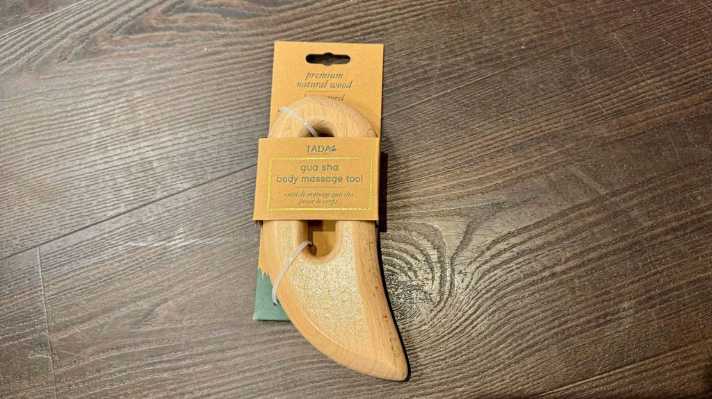 Getestete Gua Sha: Ein geglättetes Holzstück inklusive Griffmulde liegt auf einem Holzboden.