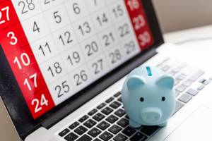 Konten fürs Tagesgeld im Test: Auf einem Laptop, der einen Kalender im Display anzeigt, steht ein hellblaues Sparschwein.