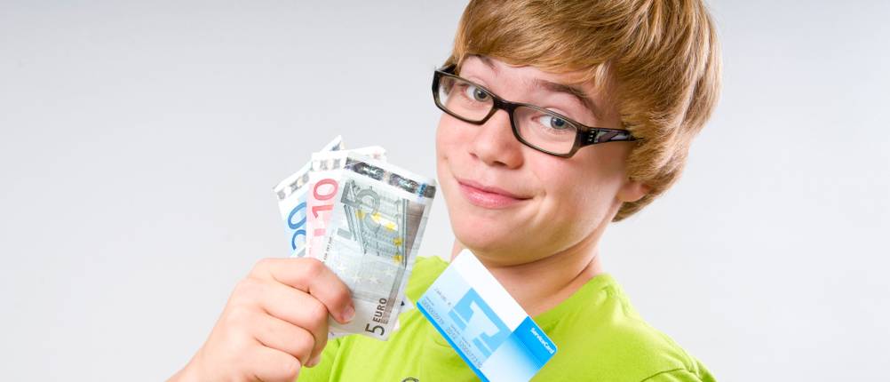 Ein Junge hält mehrere Geldscheine und die Girokarte seines Kinderkontos hoch.