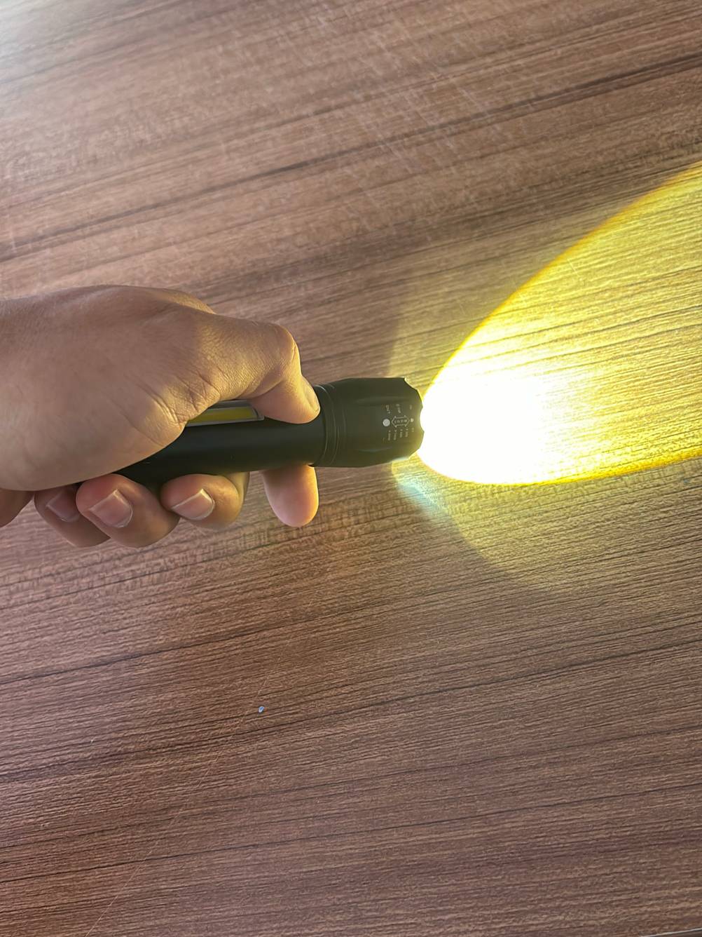Taktische Taschenlampe getestet: Eine Hand betätigt die Powertaste eines Geräts und leuchtet auf den Boden.