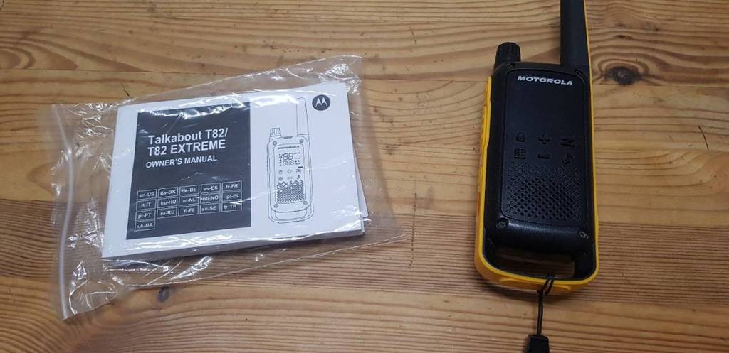 Funkgeräte-Test: Ein schwarz-gelbes Modell Talkabout T82 Extreme von Motorola liegt neben der Bedienungsanleitung auf einer Holzfläche.