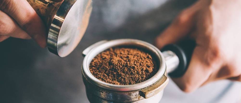 Tamper Test: Person wirkt mit einem Tamper auf einen Siebträger voller Kaffeepulver ein