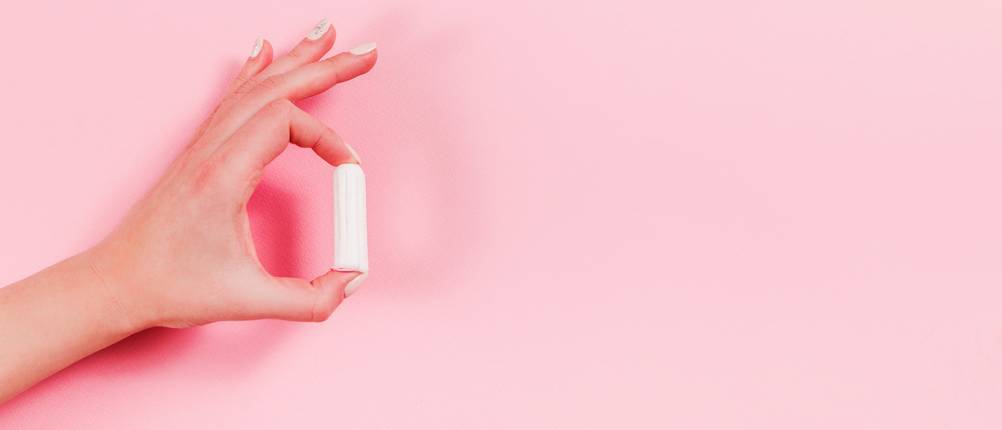 jemand hält einen Tampon vor einem pinken Hintergrund