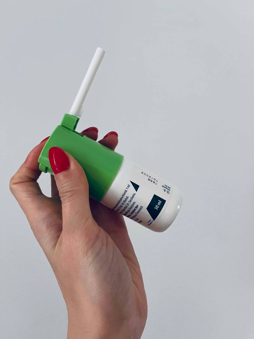 Eine Frauenhand hält ein getestetes Halsspray vor einem weißen Hintergrund.