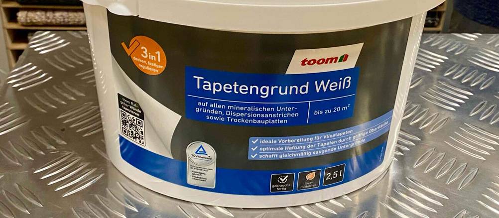 Nahaufnahme des Labels eines Kanisters des Tapetengrund (Weiß) im Test auf einer Metallfläche.
