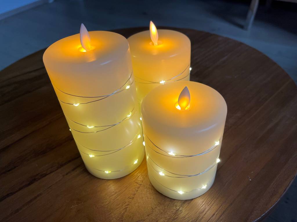 drei leuchtende LED-Kerzen auf einem Holztisch