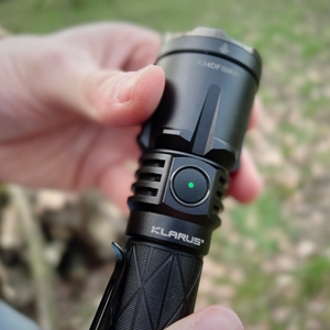 Eine Nahaufnahme des seitlichen Schalters der Klarus XT21X Pro mit einer grünen LED-Anzeige. Die Hand hält die Taschenlampe im Freien.