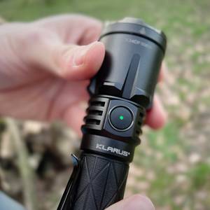 Eine Nahaufnahme des seitlichen Schalters der Klarus XT21X Pro mit einer grünen LED-Anzeige. Die Hand hält die Taschenlampe im Freien.