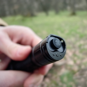 Der Heckschalter der Klarus XT21X Pro wird in Nahaufnahme gezeigt. Eine Hand hält die Taschenlampe im Freien, mit Fokus auf die Bedienelemente.