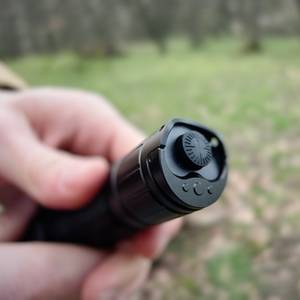 Der Heckschalter der Klarus XT21X Pro wird in Nahaufnahme gezeigt. Eine Hand hält die Taschenlampe im Freien, mit Fokus auf die Bedienelemente.