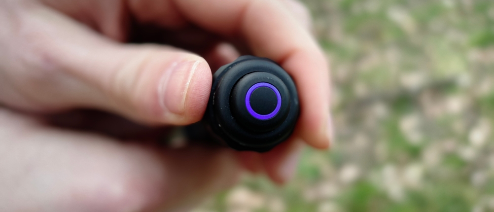 Der Heckschalter der Nextorch TA30C zeigt eine violette LED-Anzeige für den Akkustand. Eine Hand hält die Taschenlampe im Freien.