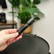 Die Nextorch TA30C Taschenlampe wird in einer Hand gehalten. Das kompakte Design mit Clip ist sichtbar.