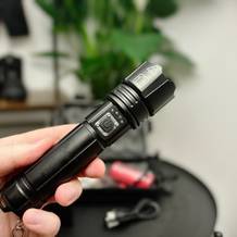 Die Shadowhawk S1476 Taschenlampe wird in einer Hand gehalten. Im Hintergrund ist ihr Zubehör zu sehen.