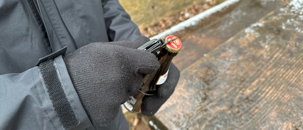 Ein Nutzer mit Handschuhen öffnet eine Bierflasche mit dem Flaschenöffner des Amazon Basics Taschenmessers. Das Messer liegt sicher in der Hand.